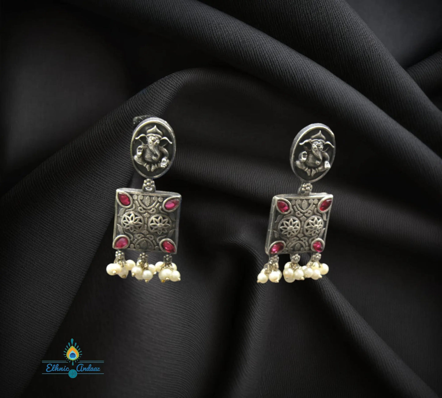 Disha oxidised necklace set featuring silver earrings with ruby stones and pearl drops on fabric background.