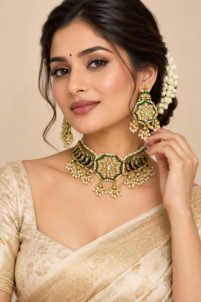 Gold and green traditional Indian jewelry set featuring a choker necklace and matching dangle earrings, displayed on a cream fabric mannequin bust with a gold stand against a wood panel and white floral background.