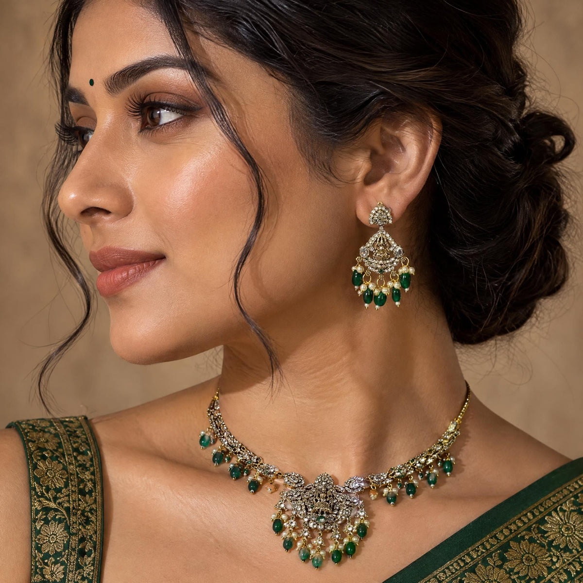 Detailed profile view of an Indian model wearing traditional gold Laxmi drop earrings with emerald bead accents.