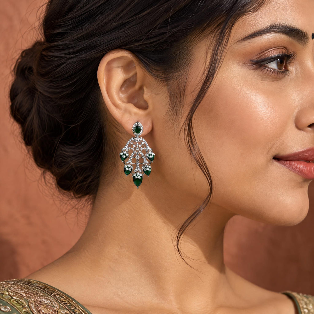 Side profile of an Indian model wearing an elegant green cubic zirconia drop earring against a muted terracotta background.