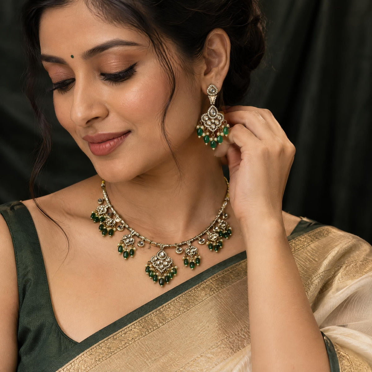 Macro view of an ornate kundan bangle with emerald beads showcased against a dark matte silk fabric background.