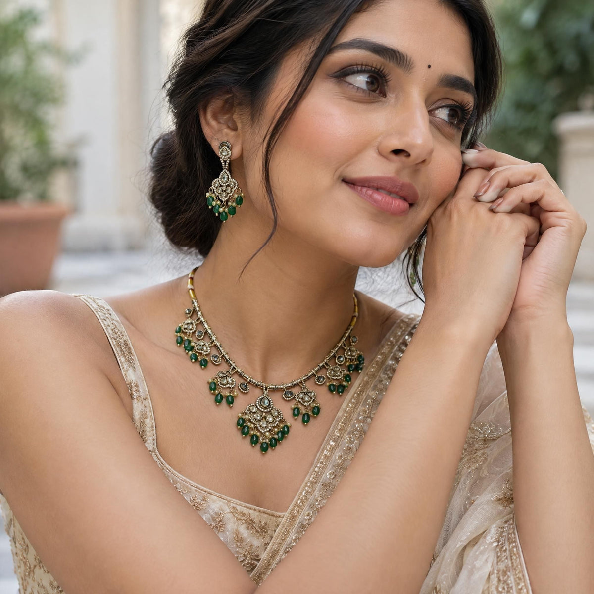 Low-angle shot of an Indian model's hands resting near her face, highlighting the intricate kundan and emerald bead design.
