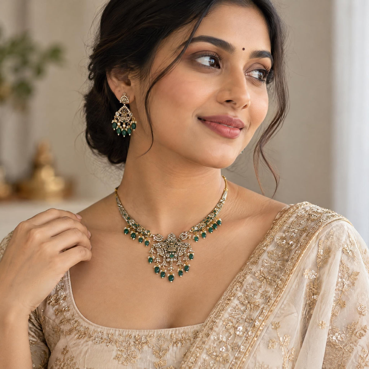 Indian model wearing an elegant gold Laxmi pendant necklace with a rich emerald bead center in a soft-lit interior.