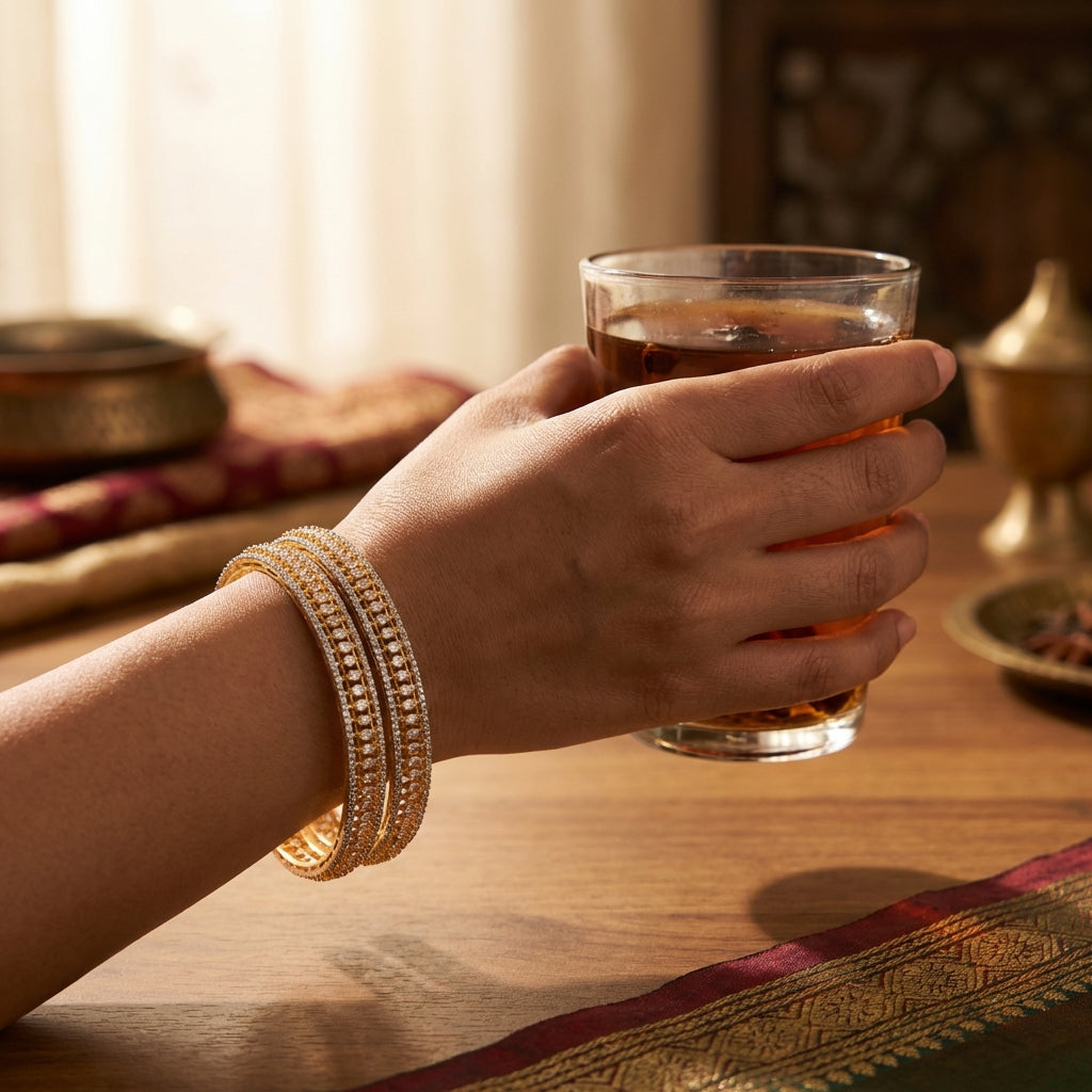 Close-up of Indian woman's hand holding tea glass, decorated with a tiny Teji CZ bangle in warm indoor lighting, highlighting elegance.