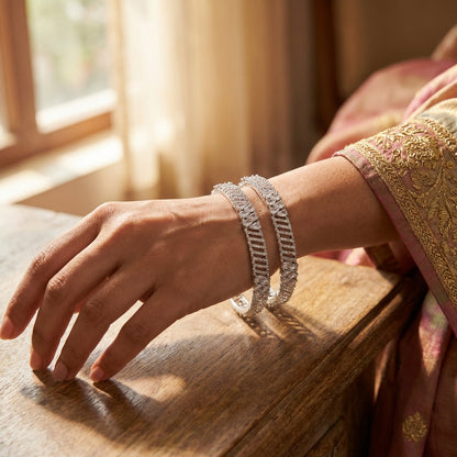 Stylish indoor setting with a minimalistic marble countertop displaying a miniature Kamala CZ bangle, accented with a white flower and reflected surface.