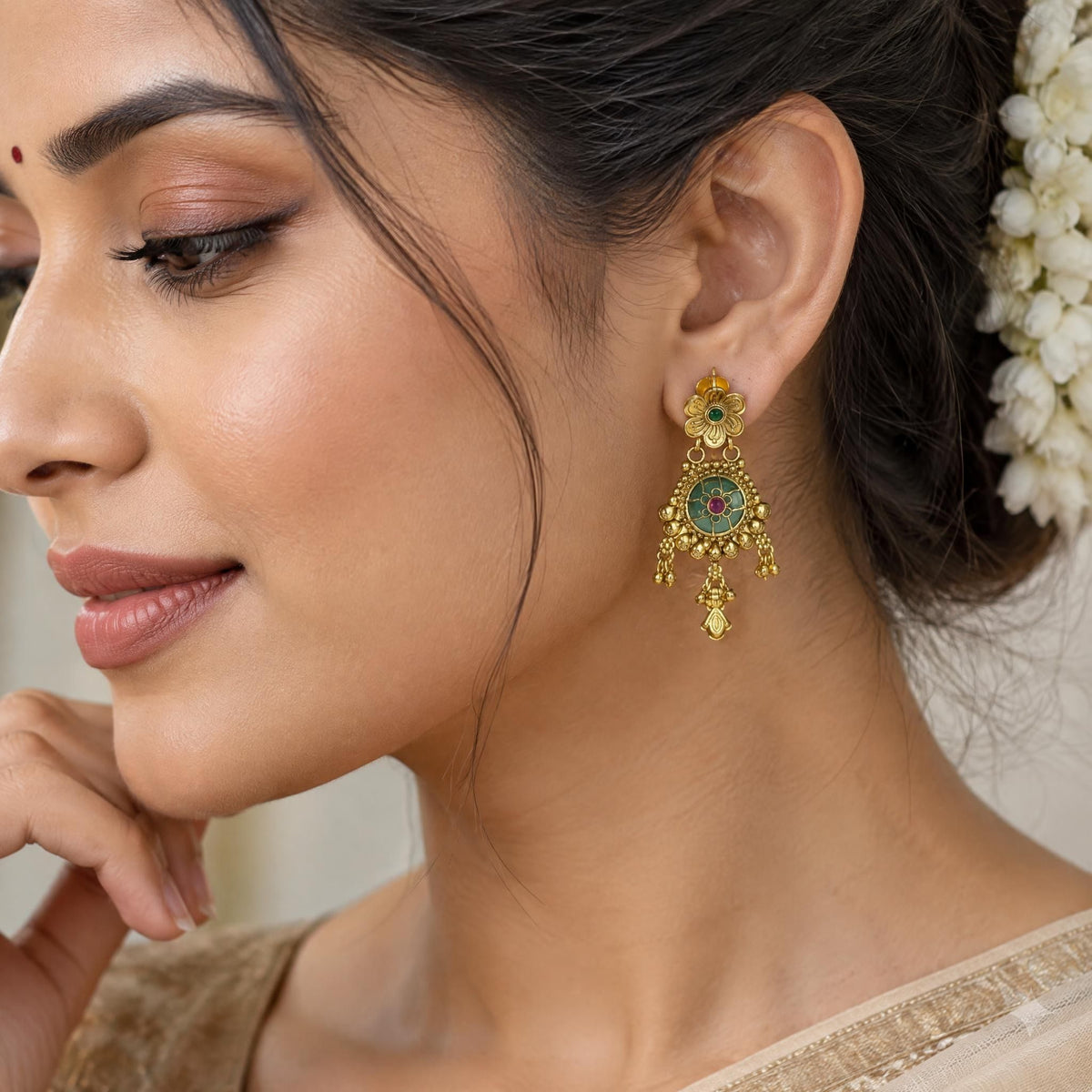 Profile close-up of a gold earring with ruby and emerald inlay worn by an Indian model.
