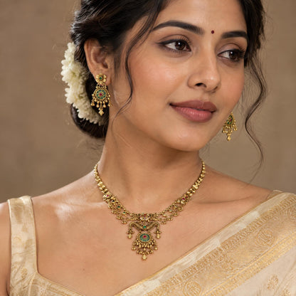 Indian model wearing a gold necklace with ruby and emerald accents in a close-up portrait.